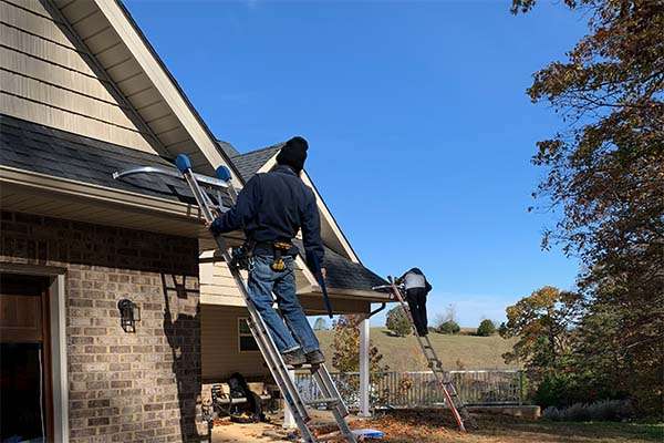 two installers on ladders checking the pitch of the gutters with levels before installing gutter guards